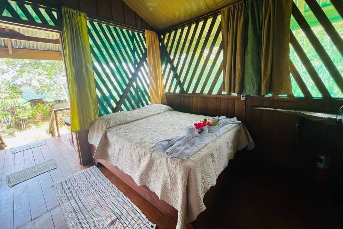 A room with a bed, wooden walls, and a window with striped curtains.