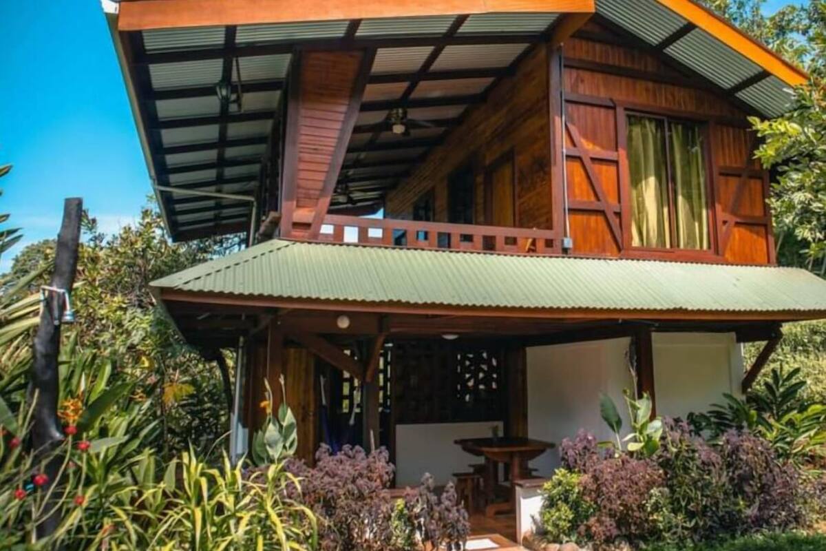 A two-story wooden house with a covered porch and a small garden area.