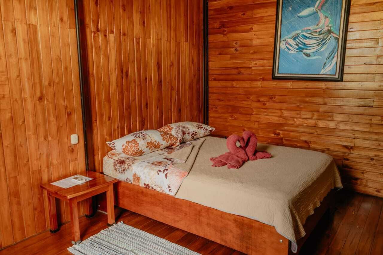 A wooden-paneled room with a bed, a small table, and a framed painting on the wall.