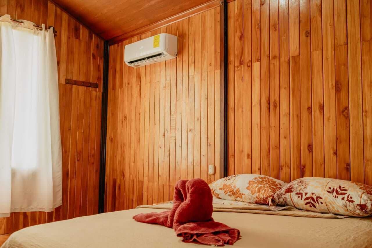 A wooden-paneled room with a bed, a red towel, and an air conditioning unit.