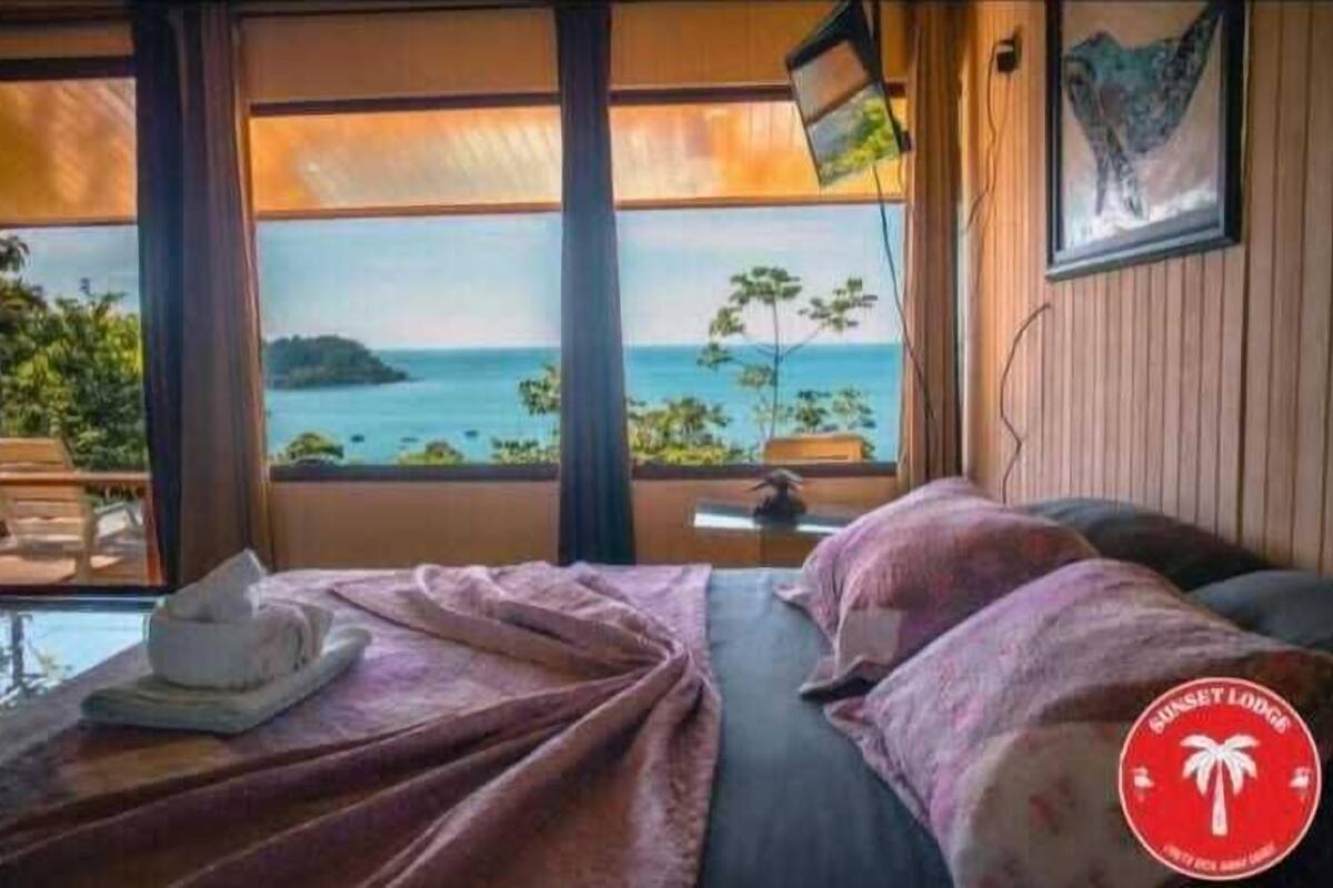 A room with a bed, a view of the sea, and a logo on the wall.