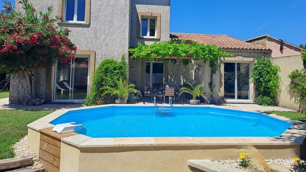 A two-story house with a swimming pool, outdoor seating, and a pergola covered with greenery.
