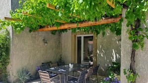 An outdoor patio with a table and chairs, surrounded by greenery and a pergola.