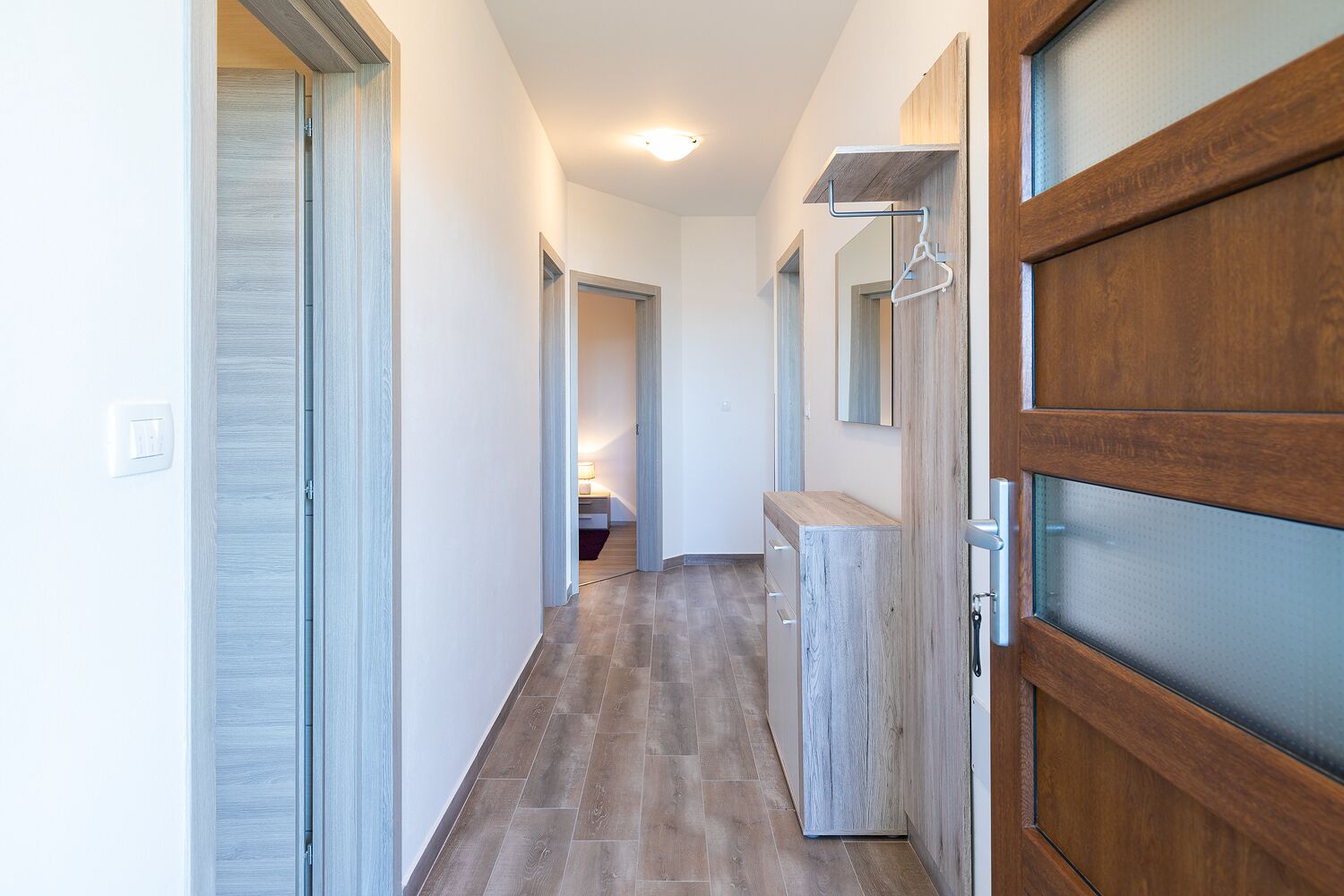 Un pasillo con una puerta de madera, un espejo y un banco de madera.