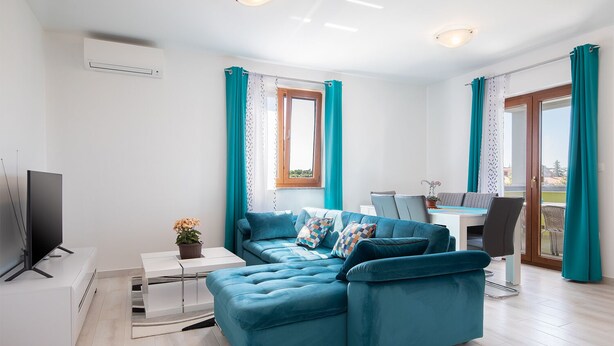 A modern living room with a sectional sofa, a flat-screen TV, a dining area with a table and chairs, and a balcony with curtains. - Kaylie Apartment, 3 bedroom place in Pula, Croatia (Pula)