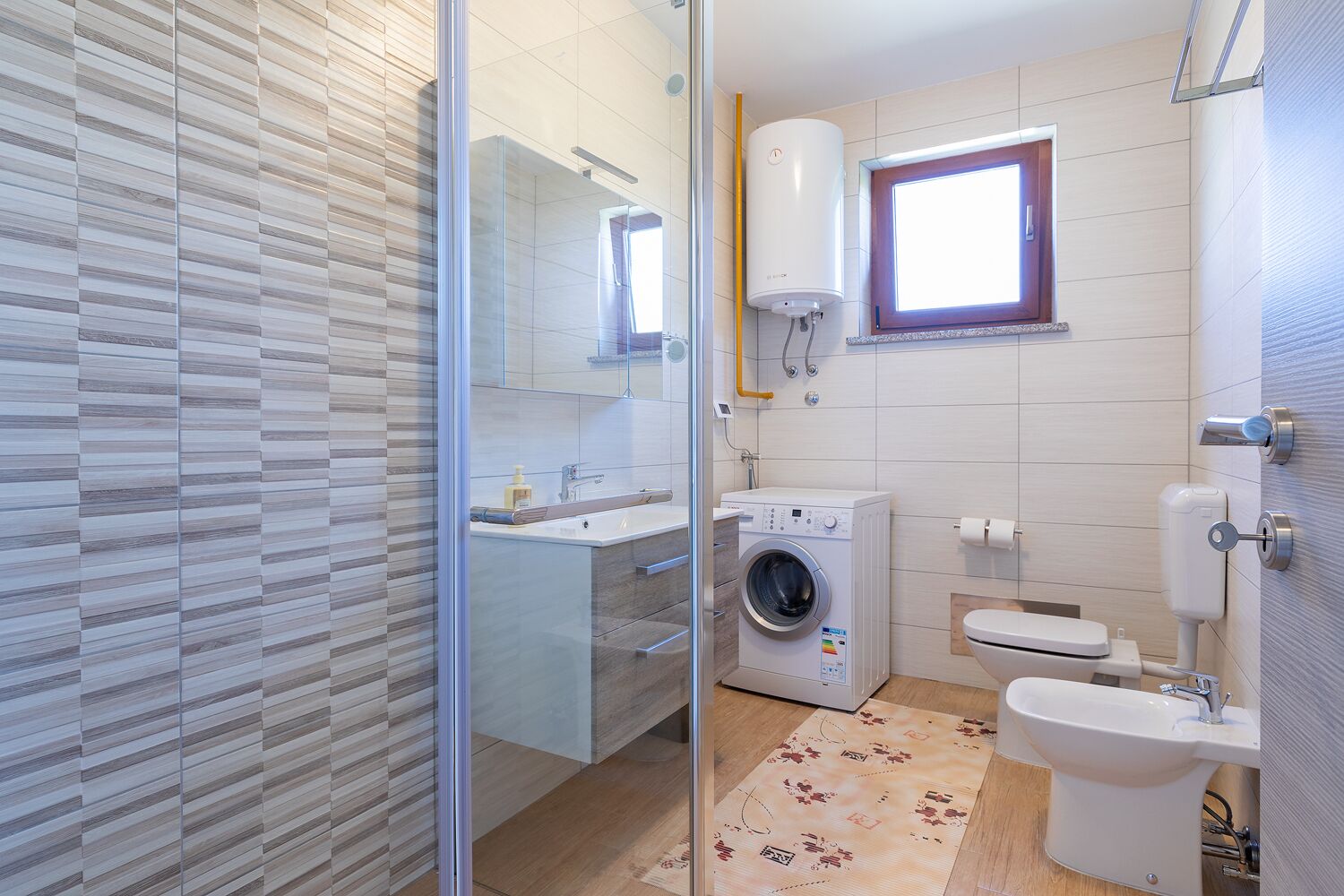 A modern bathroom with a glass shower enclosure, a built-in washing machine, a toilet, and a sink with a mirror.