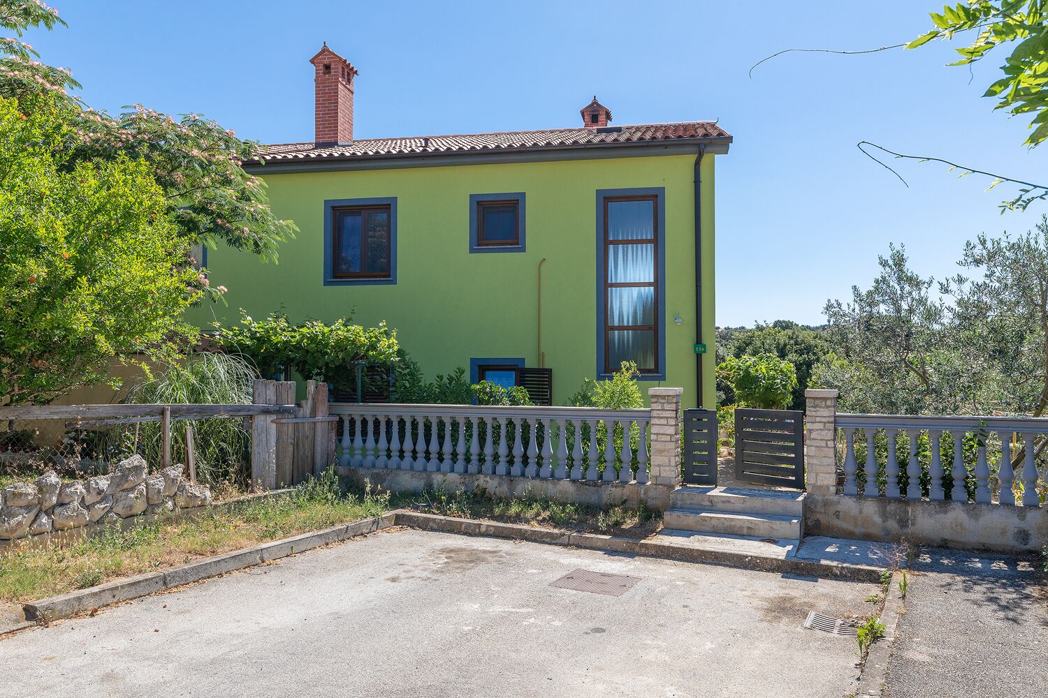 A two-story house with a green facade, a brick chimney, and a gated entrance.