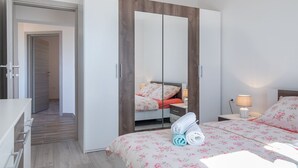 A bedroom with a wardrobe, a bed with floral bedding, a bedside table with a lamp, and a towel on the bed. - Kaylie Apartment, 3 bedroom place in Pula, Croatia (Pula)