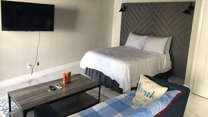 A bedroom with a bed, a TV mounted on the wall, a coffee table, and a couch. - Beach Hideaway (Nassau)
