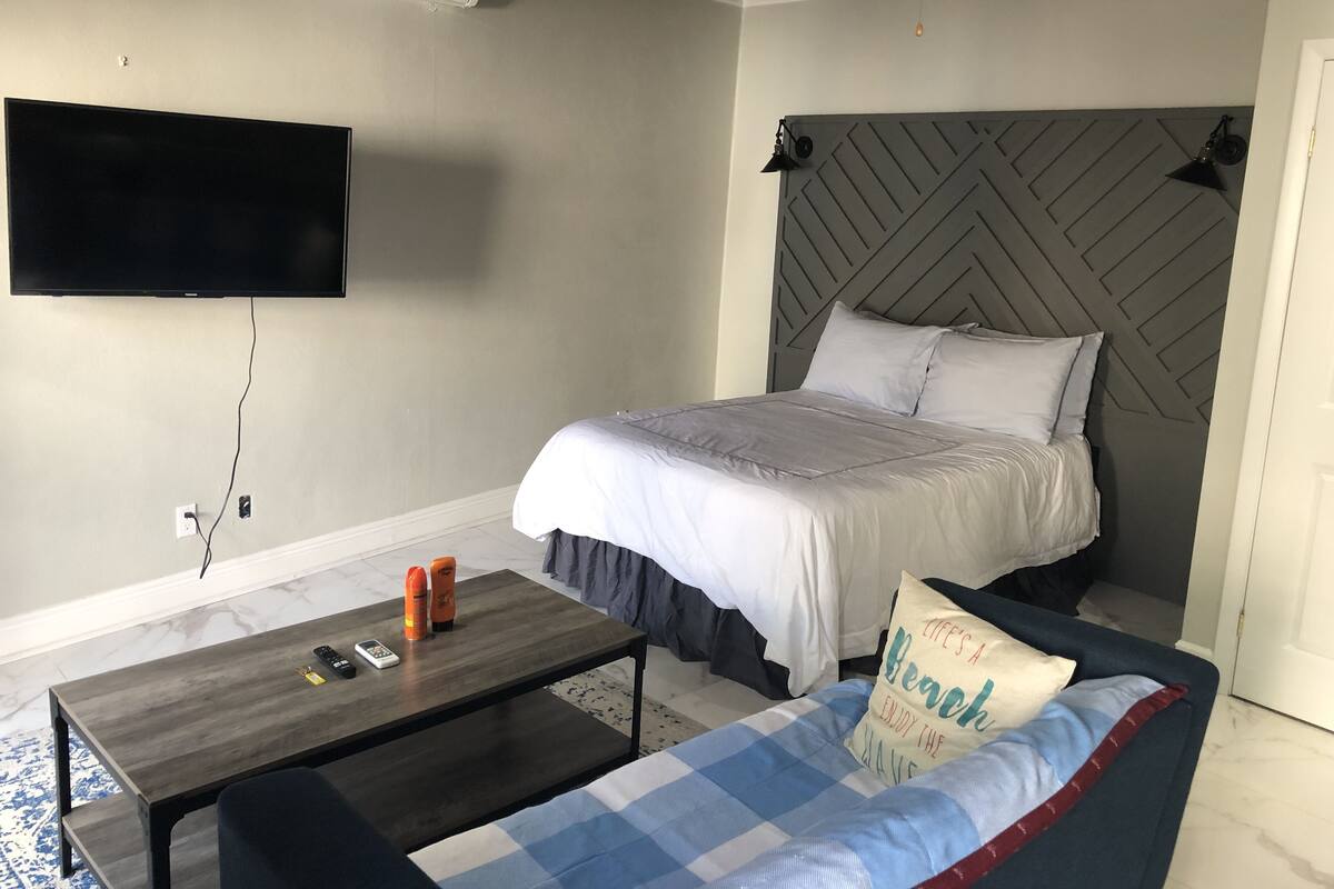Un dormitorio con cama, televisor montado en la pared, una mesa de centro y un sofá.