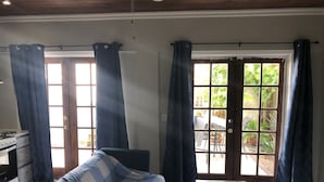 A room with a checkered sofa, a small table with a remote control, and a view of an outdoor garden through a glass door. - Beach Hideaway (Nassau)