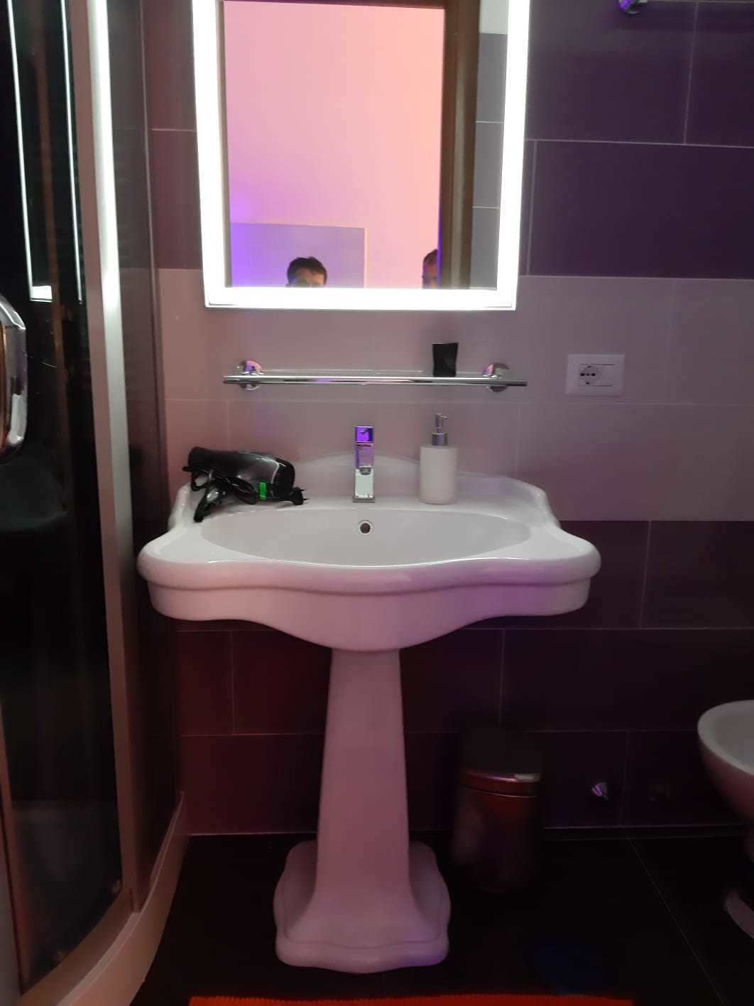 A bathroom with a pedestal sink, a mirror, and a shower area.