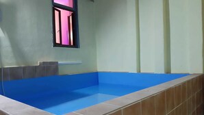 A room with a blue-tiled pool, a window with pink framing, and a white shelf. - Modina Guest House (Rome)