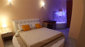 A circular bed with a headboard, two orange pillows, a bedside table with a lamp, and a bathroom with a bathtub and a shower. - Modina Guest House (Rome)
