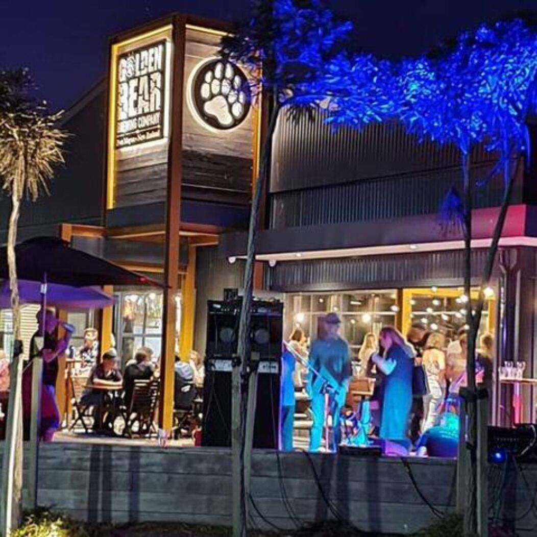 An outdoor seating area with tables and chairs, a stage for performances, and a sign for "Golden Bear."