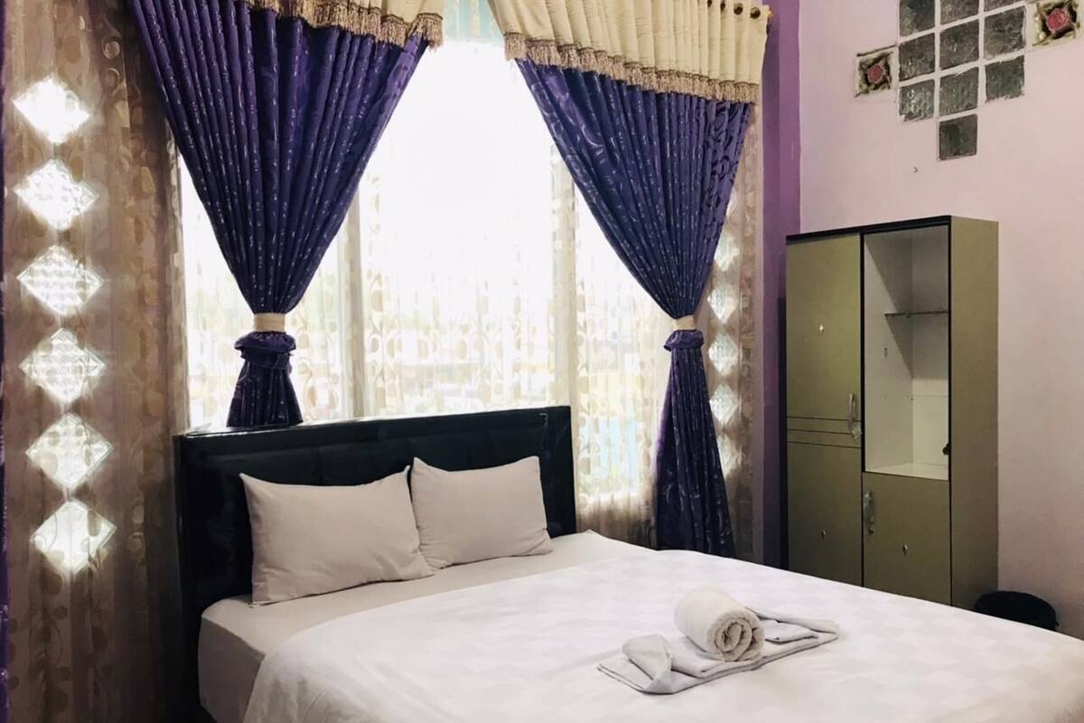 A neatly made bed with white linens, a headboard, and a rolled towel on the bed.