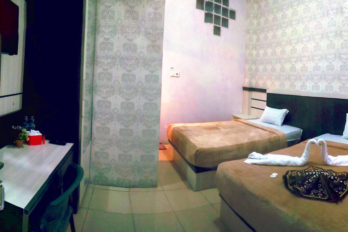 A hotel room with two beds, a small table with a red object, and patterned wallpaper.