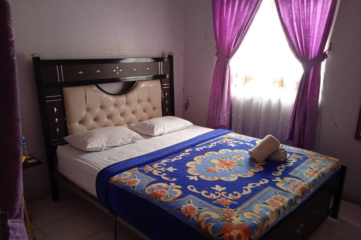 A bed with a tufted headboard, white bedding, and a blue floral bedspread.