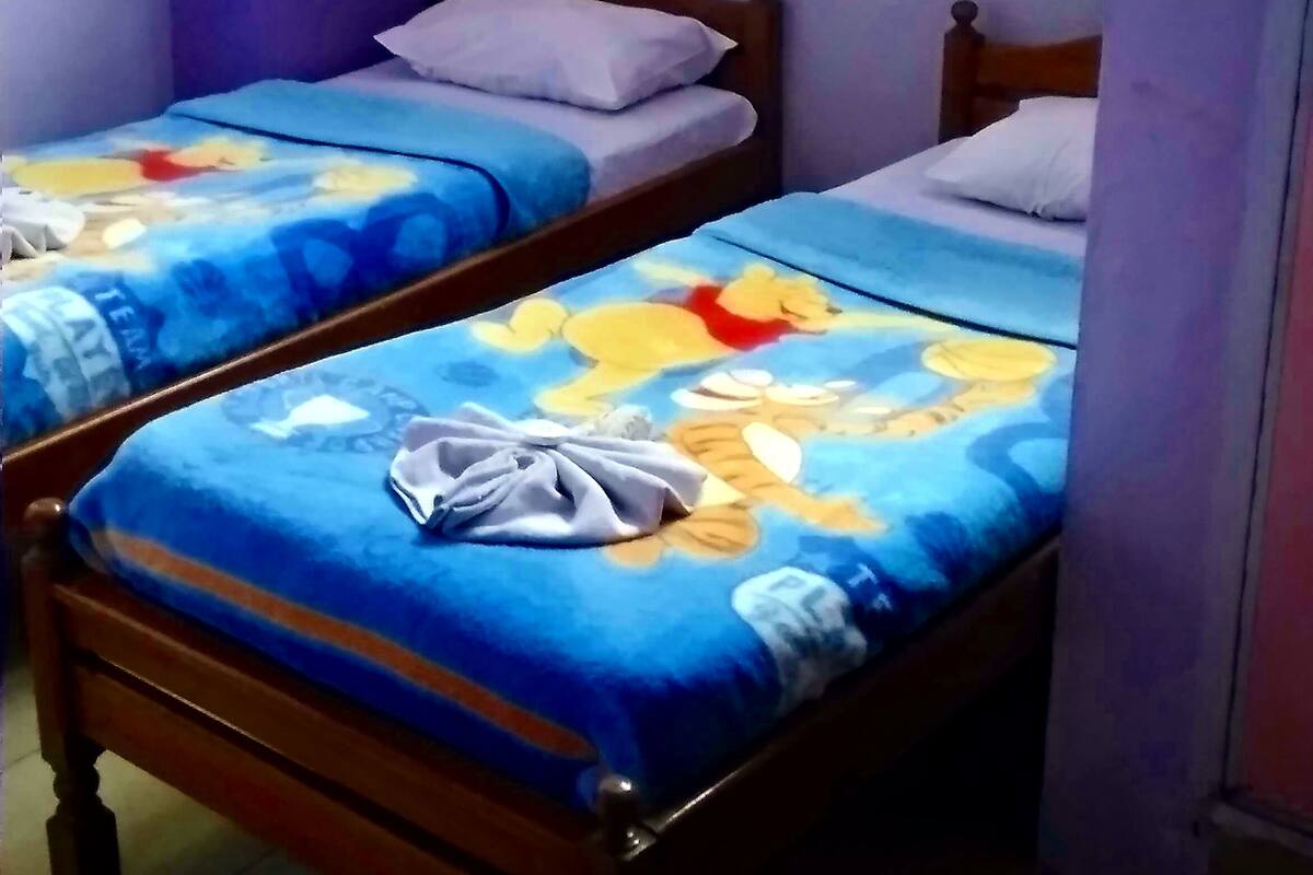 A small, dimly lit room with two wooden beds, each with a colorful bedspread and pillows.