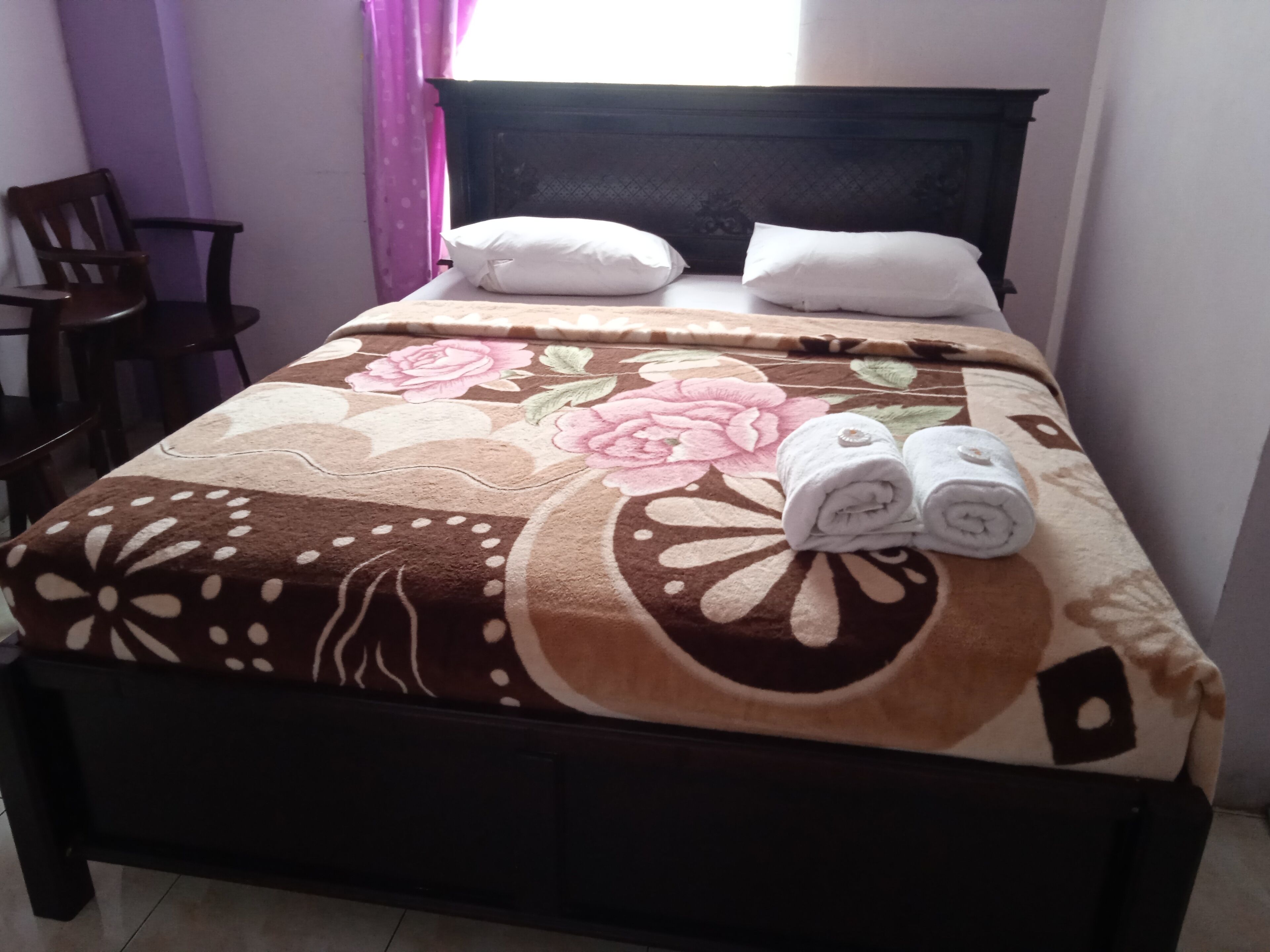 Una cama con una colcha estampada de flores, dos almohadas y dos toallas enrolladas.