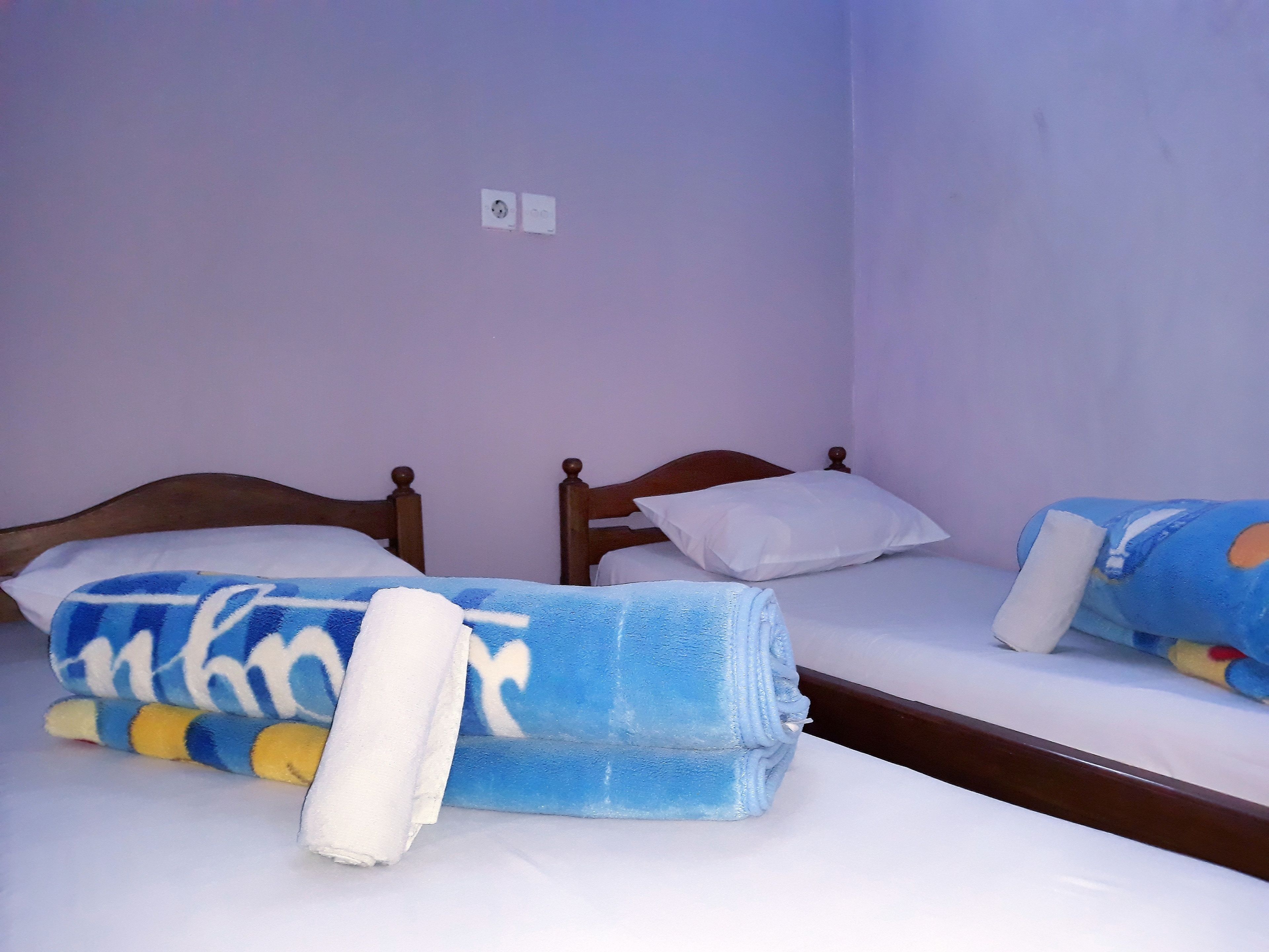 Two single beds with wooden headboards in a room with light purple walls.