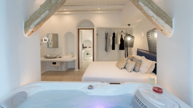 A modern bedroom with a large bed, a sitting area with a view of the bathroom, and a hot tub. - Euphoria Downtown (Naxos)