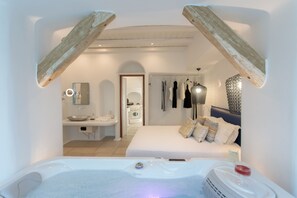 Une chambre moderne avec un grand lit, un coin salon donnant sur la salle de bain et un jacuzzi.