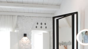A bathroom with a stone wall, a bathtub, a large mirror, and a sink with a bowl. - Euphoria Downtown (Naxos)
