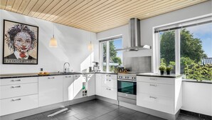 A modern kitchen with white cabinetry, a stainless steel range hood, and a large window providing a view of the outdoors. - Pet friendly home in Børkop with WiFi (Børkop)
