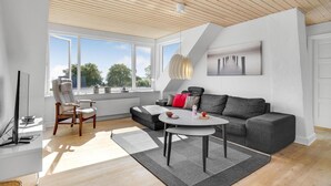 A modern living room with a grey sofa, a round coffee table, and a large window offering a view of trees and buildings. - Pet friendly home in Børkop with WiFi (Børkop)