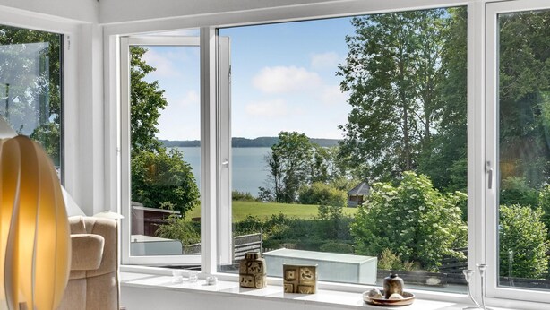 A room with a large window overlooking a lake, a chair, and decorative items on the windowsill. - Pet friendly home in Børkop with WiFi (Børkop)