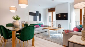 Un salon moderne avec un canapé, des fauteuils verts, une table basse et un téléviseur.