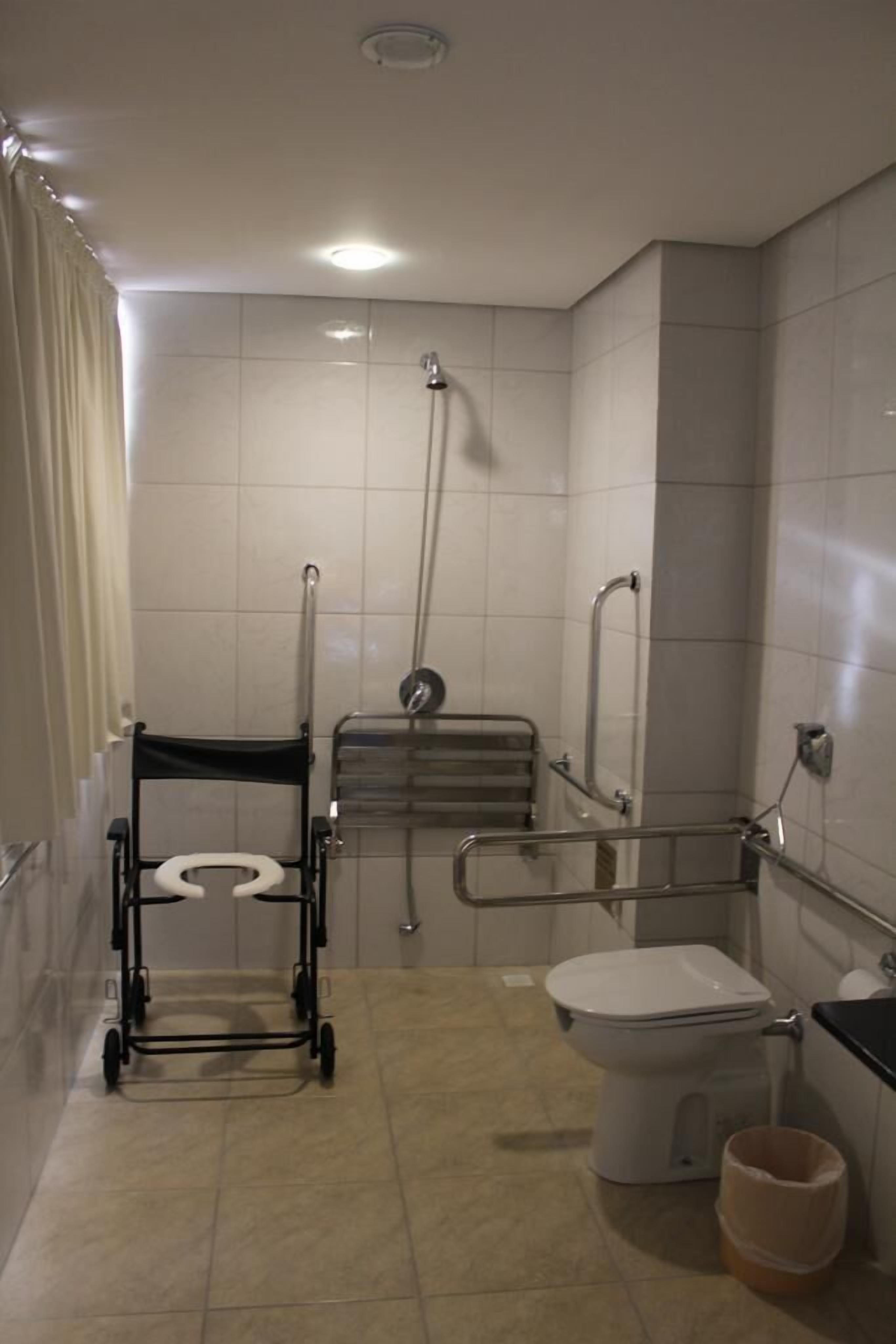 Baño accesible para sillas de ruedas, con inodoro, barras de apoyo, asiento de ducha y pasamanos.