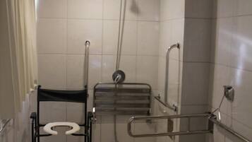 Baño accesible para sillas de ruedas, con inodoro, barras de apoyo, asiento de ducha y pasamanos.