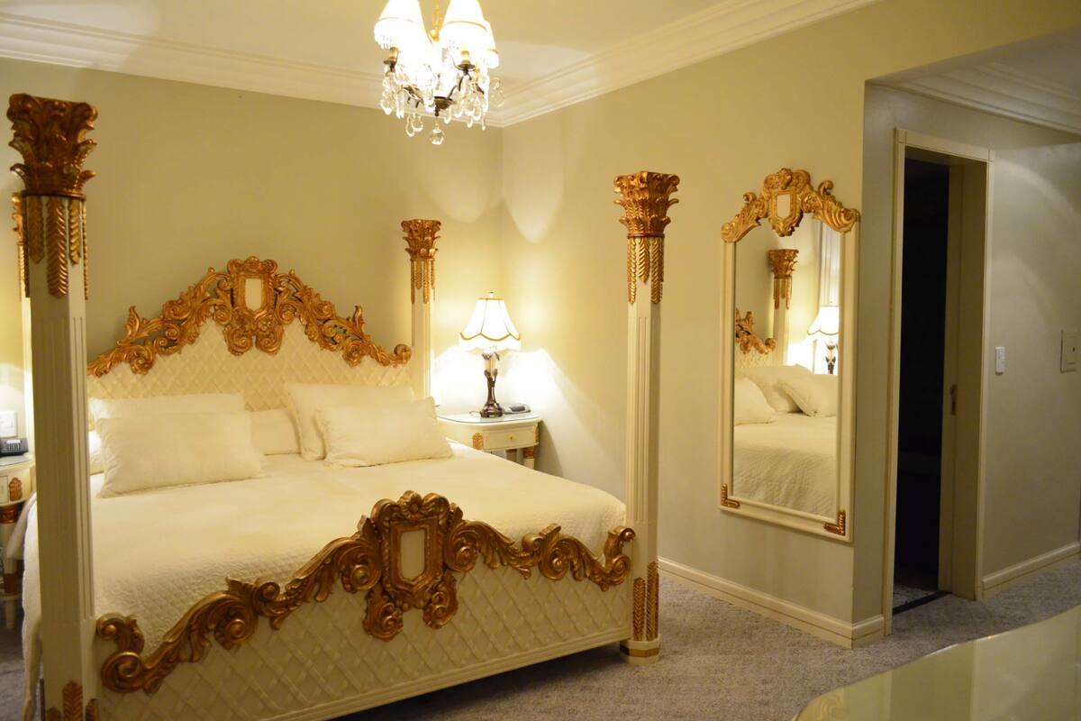 A luxurious bedroom with an ornate four-poster bed, a large mirror, and a chandelier.