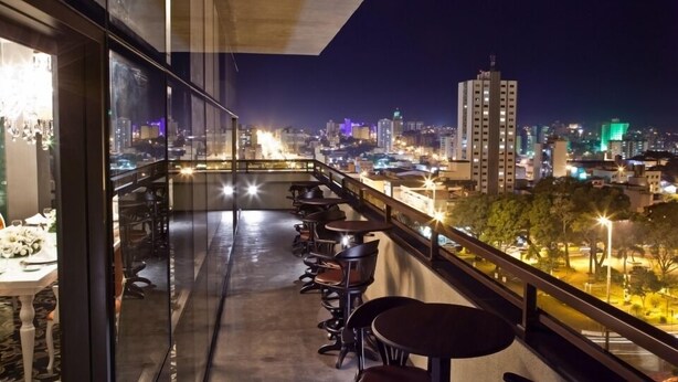 Un balcon avec des tables et des chaises, d’où l’on peut admirer la vue sur la ville illuminée la nuit.