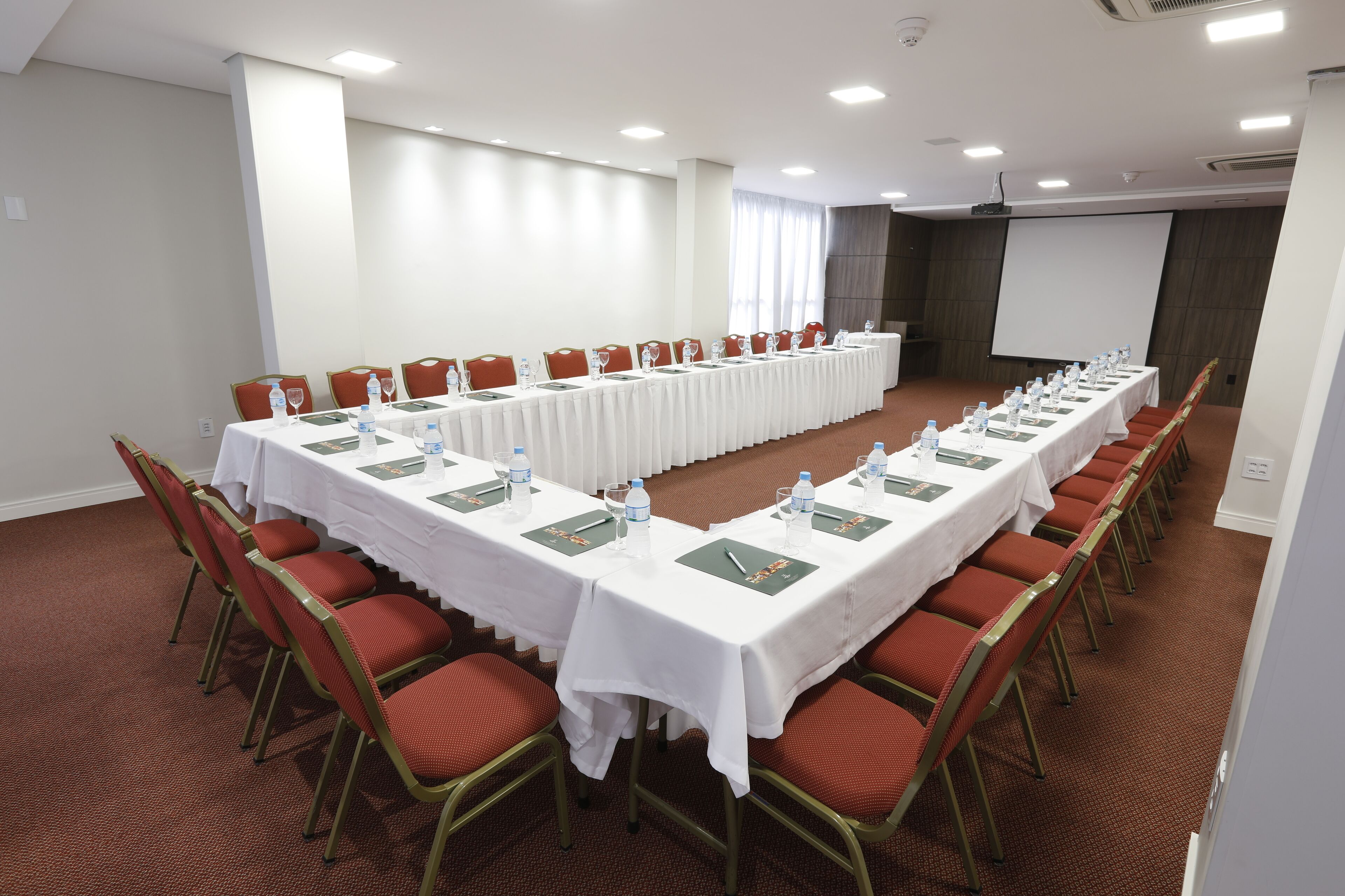 A conference room with a long table, red chairs, white tablecloths, water bottles, and nameplates.