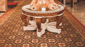 Un ours en peluche moelleux est posé sur une table décorative dans le hall d'un hôtel, où l'on peut également admirer un lustre, une moquette à motifs et un comptoir d'accueil.