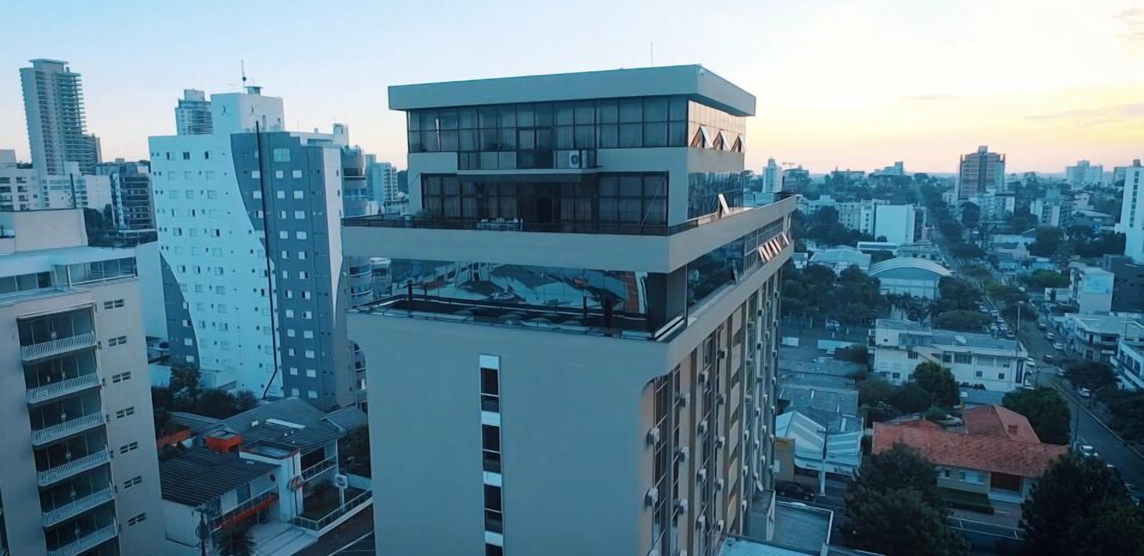 A modern high-rise building with a rooftop terrace, surrounded by other buildings in an urban setting.