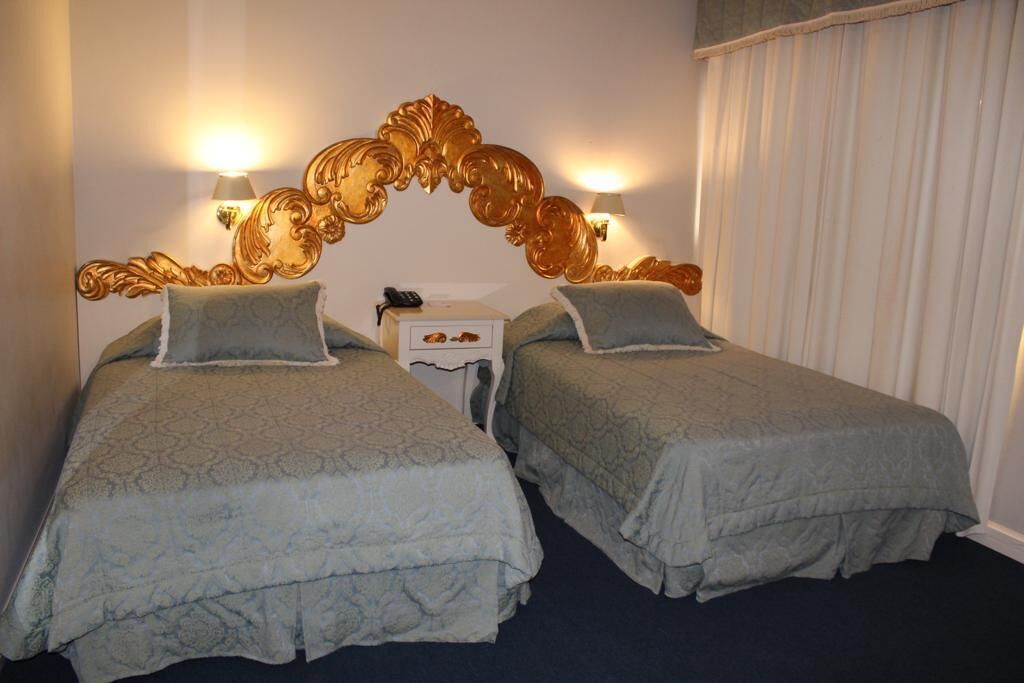 Habitación doble con dos camas, cada una con una colcha estampada, una mesita de noche con lámpara y un cabecero decorativo.