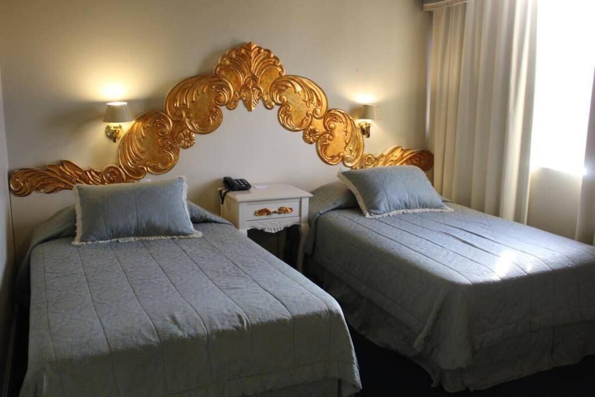 A hotel room with two single beds, a decorative headboard, bedside lamps, and a nightstand with a phone.