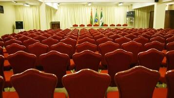 Un salón de conferencias con hileras de sillas rojas, un atril y banderas en la pared.