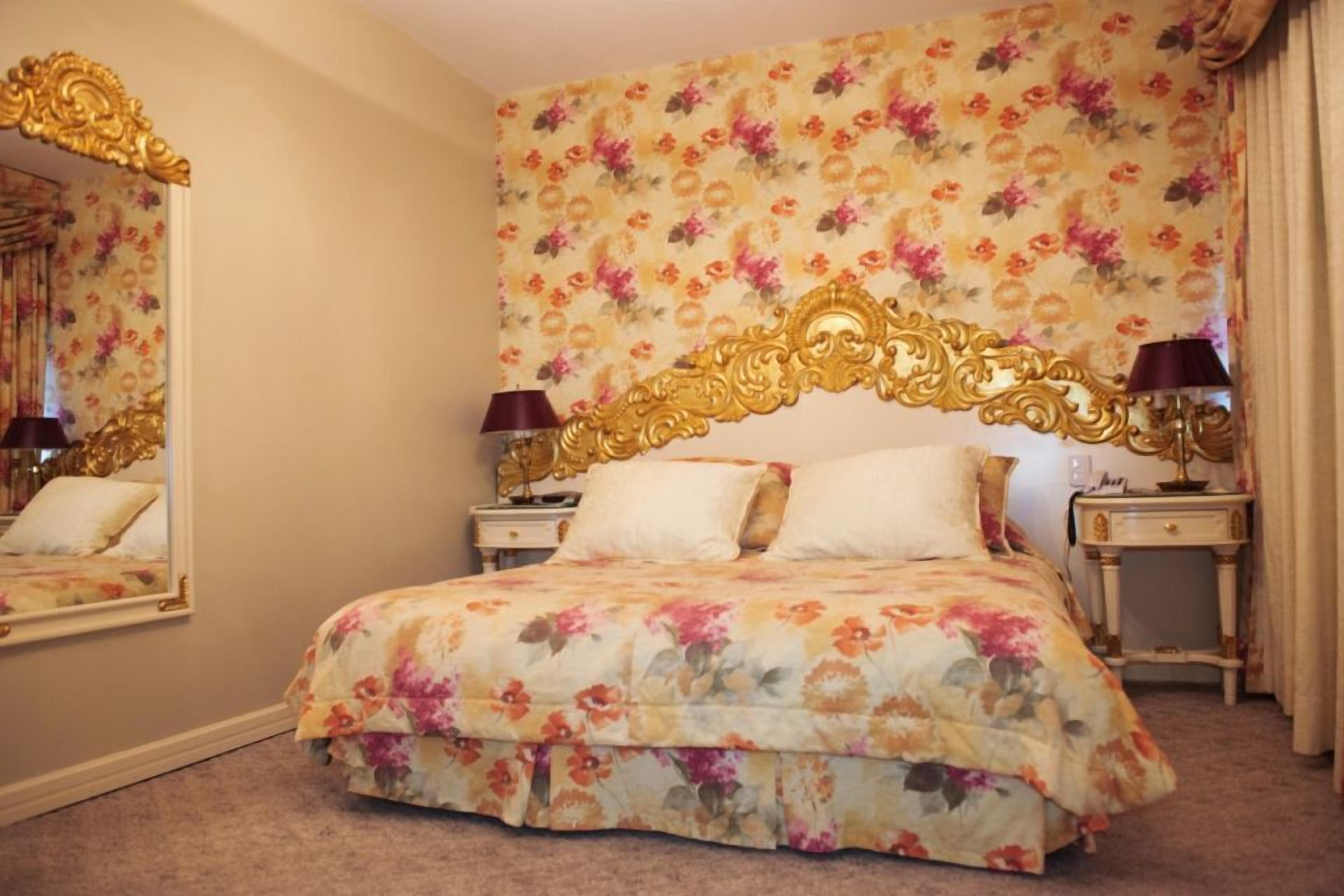 A bedroom with a floral bedspread, a gold-framed headboard, and a mirror on the wall.