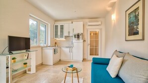 A compact living space with a kitchenette, a TV on a glass table, and a blue sofa.