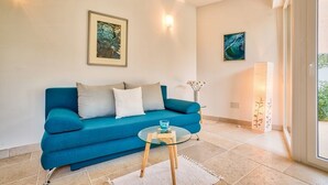 A modern living room with a teal sofa, a glass coffee table, and two framed artworks on the wall.
