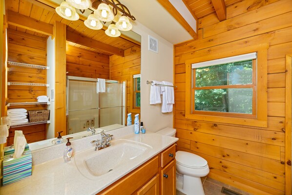 A wooden cabin bathroom with a large mirror, double sink, and a window with a view of trees.