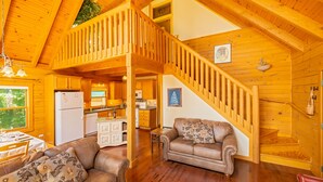 L’intérieur d’une cabane en bois comprend un coin repas, une cuisine, un salon et un escalier menant à un niveau supérieur.