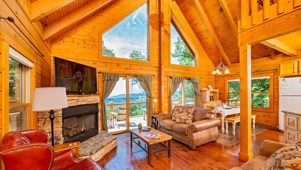 Une cabane en bois spacieuse, dotée d’une cheminée, de sièges en cuir et de grandes fenêtres offrant une vue sur l’extérieur.