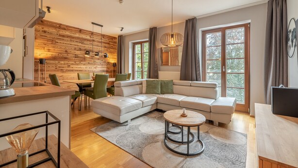Een moderne woonkamer met een hoekbank, een ronde salontafel en een eethoek met een wand van hout.