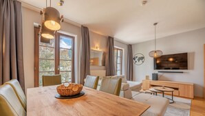 Een moderne woonkamer met een houten eettafel, lederen stoelen, een bank en een aan de muur bevestigde televisie.